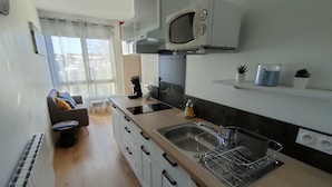 A modern kitchen with a built-in microwave, a sink, and a dish rack. There is a small seating area with a sofa and a coffee table. - Bel Appartement au Bord de L'océan (Saint-Jean-de-Monts)