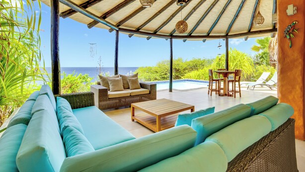 Un área de estar al aire libre techada con piscina, sillones de descanso y vista al océano.