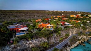 Un complejo turístico costero con villas, una piscina y una carretera serpenteando por terreno rocoso.