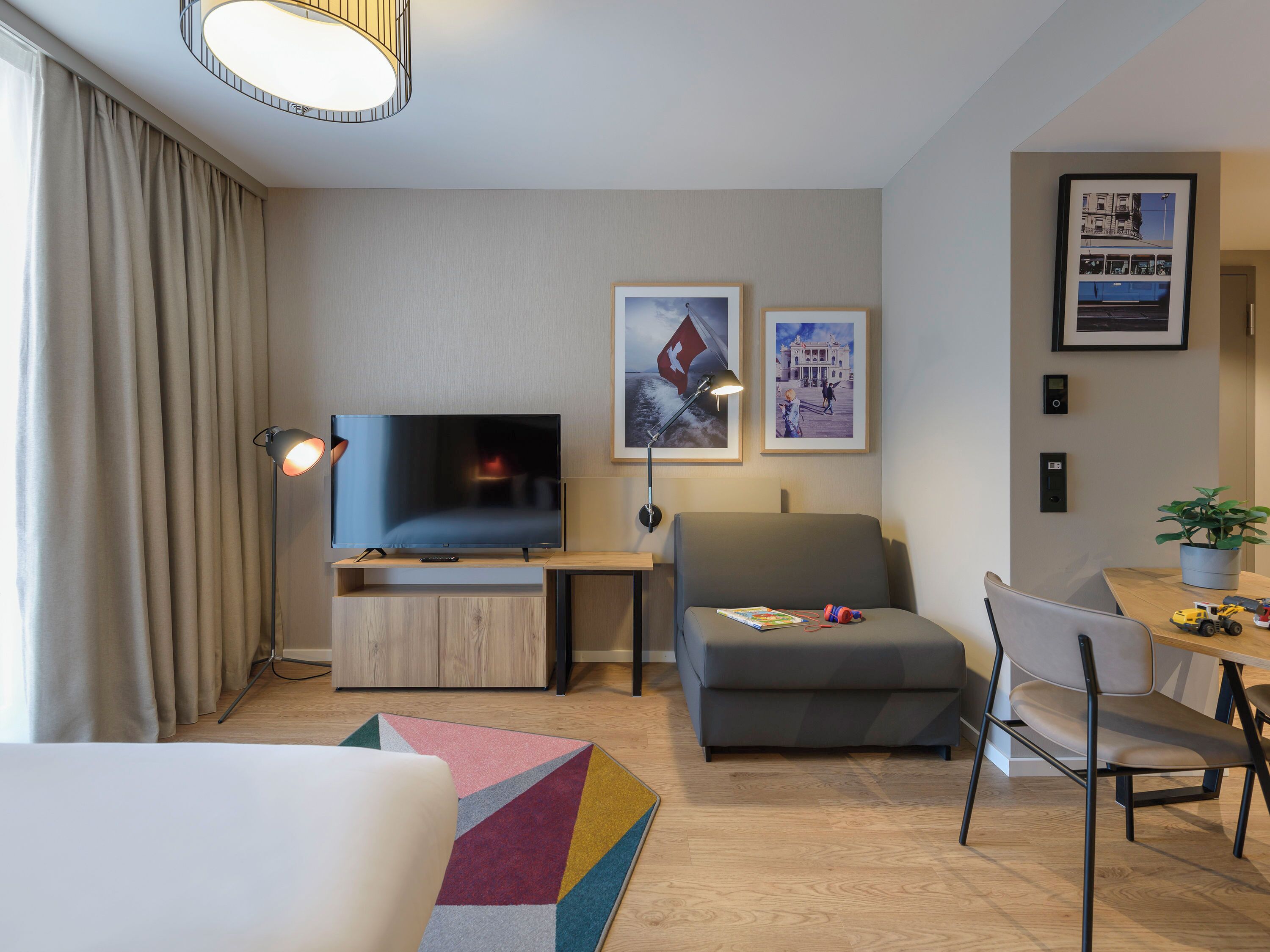 A modern living room with a flat-screen TV, a sofa, a dining table with chairs, and a colorful rug.