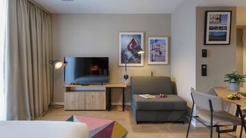 A modern living room with a flat-screen TV, a sofa, a dining table with chairs, and a colorful rug.
