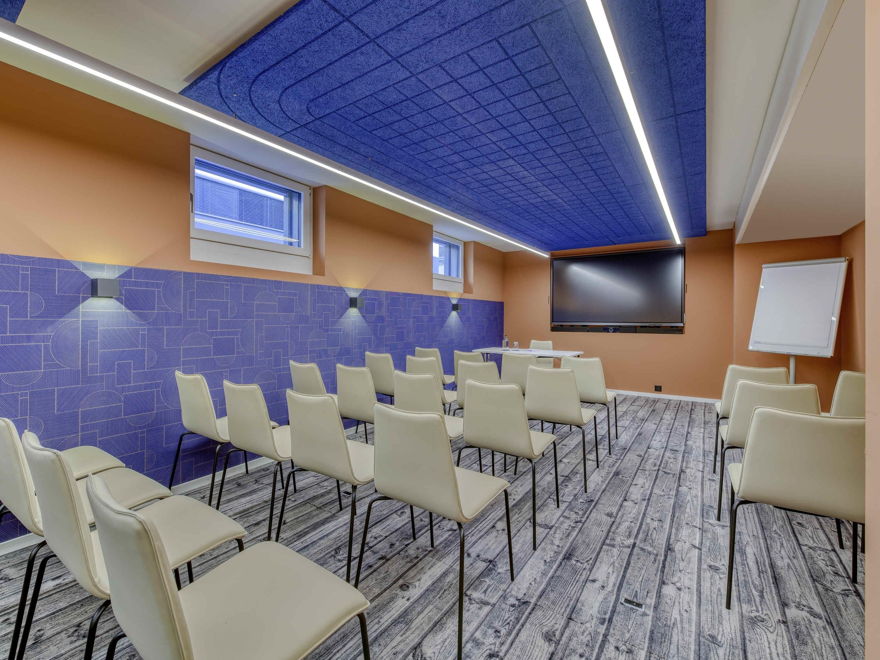 Una sala de conferencias con una pared de diseño geométrico, una pantalla grande y una pizarra.