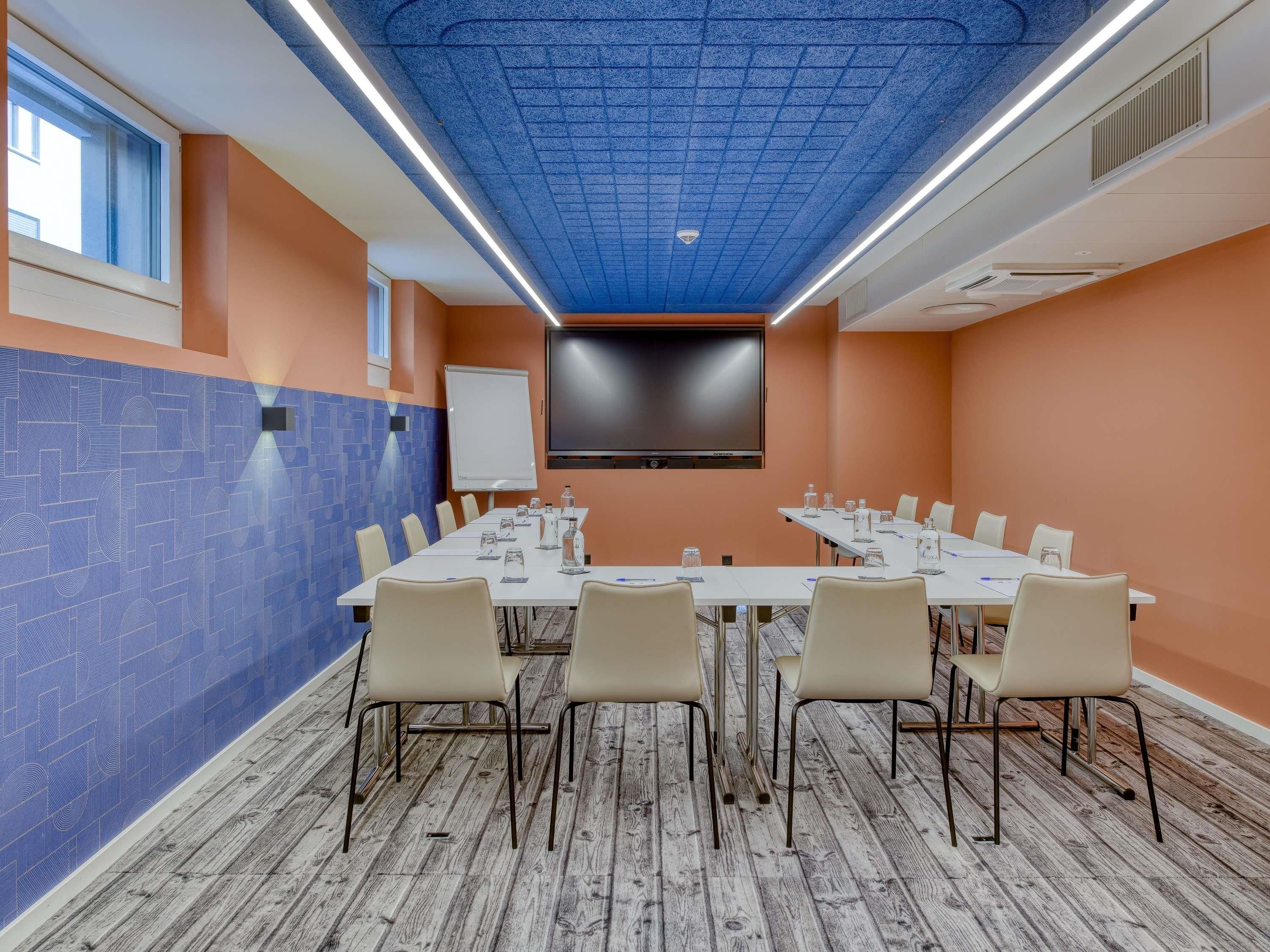 A conference room with a long table, chairs, a whiteboard, a flat-screen TV, and a patterned wall.
