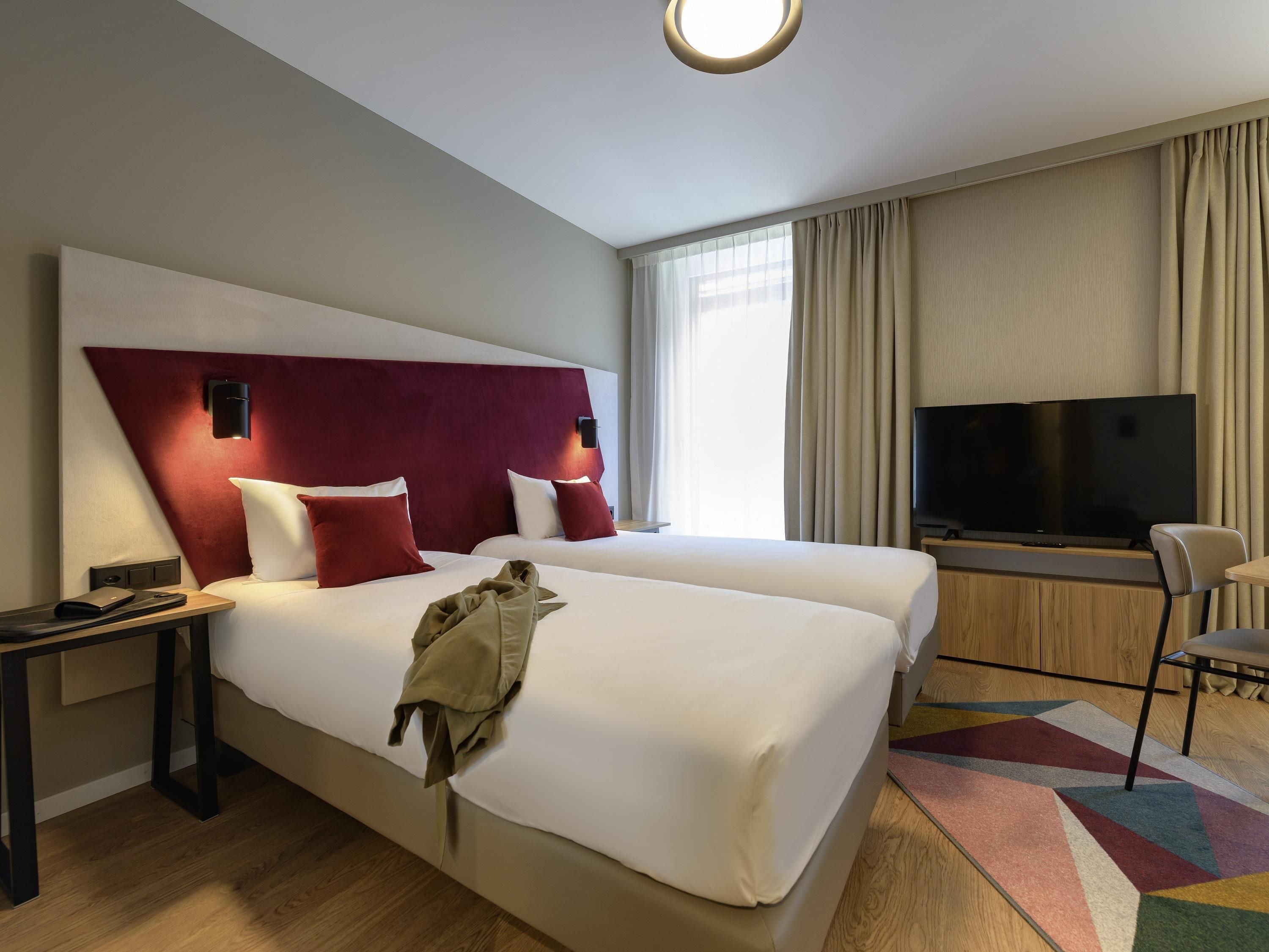 A hotel room with two beds, a television, a desk, and a chair.