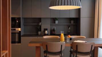 Une cuisine moderne avec un coin repas, comprenant une table en bois, deux chaises, un luminaire suspendu et une machine à café.