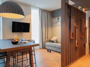 Una sala moderna con comedor, un televisor de pantalla plana montado en la pared, un sofá y un separador de madera.