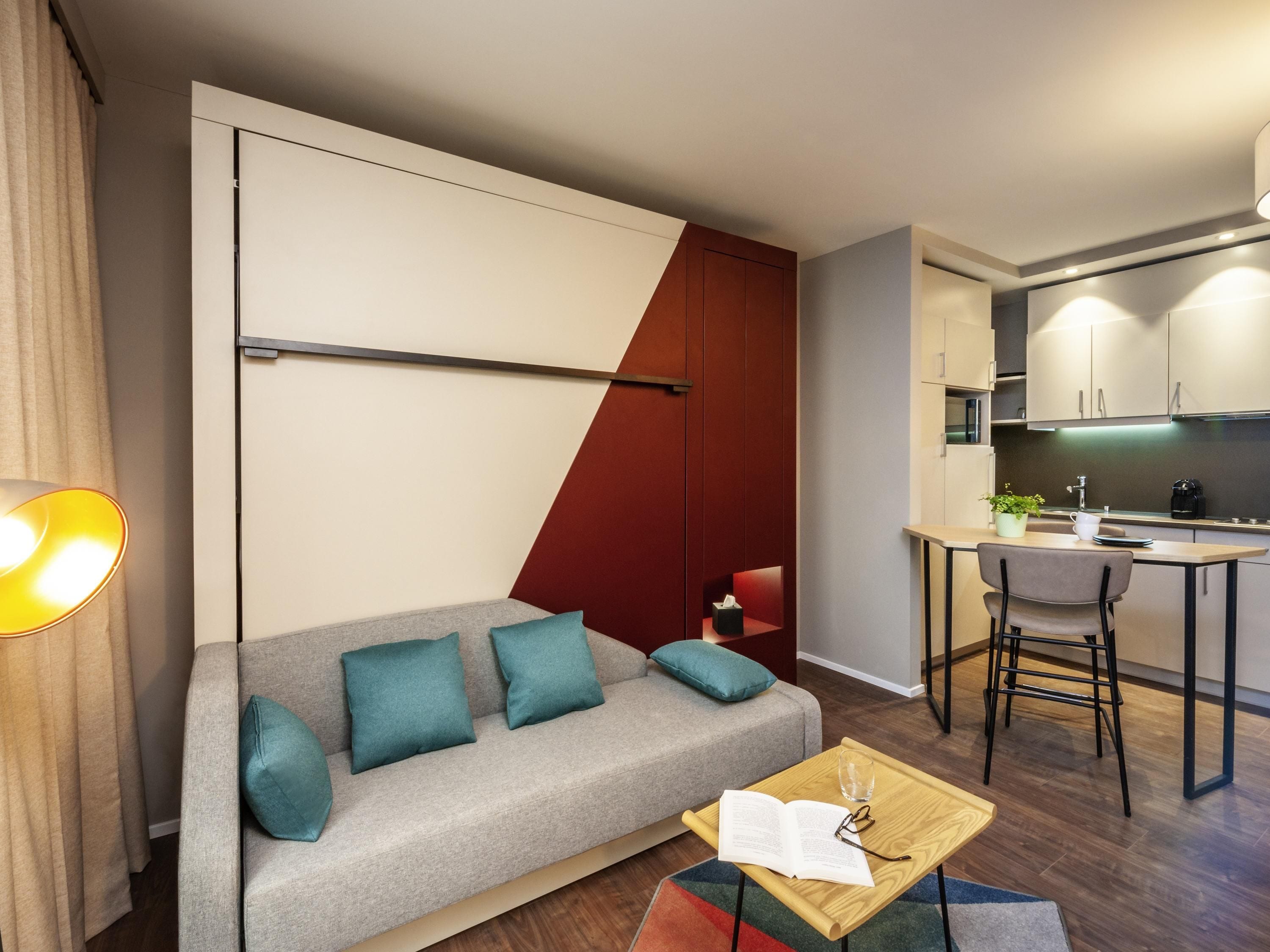 Un salon moderne comprenant un canapé, une petite table basse et un coin cuisine avec une table à manger et des tabourets de bar.