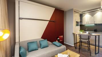 Un salon moderne comprenant un canapé, une petite table basse et un coin cuisine avec une table à manger et des tabourets de bar.