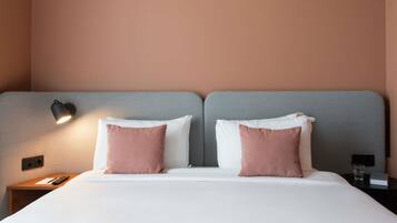 A double bed with two pillows, a bedside table with a remote control, and a wall-mounted lamp.