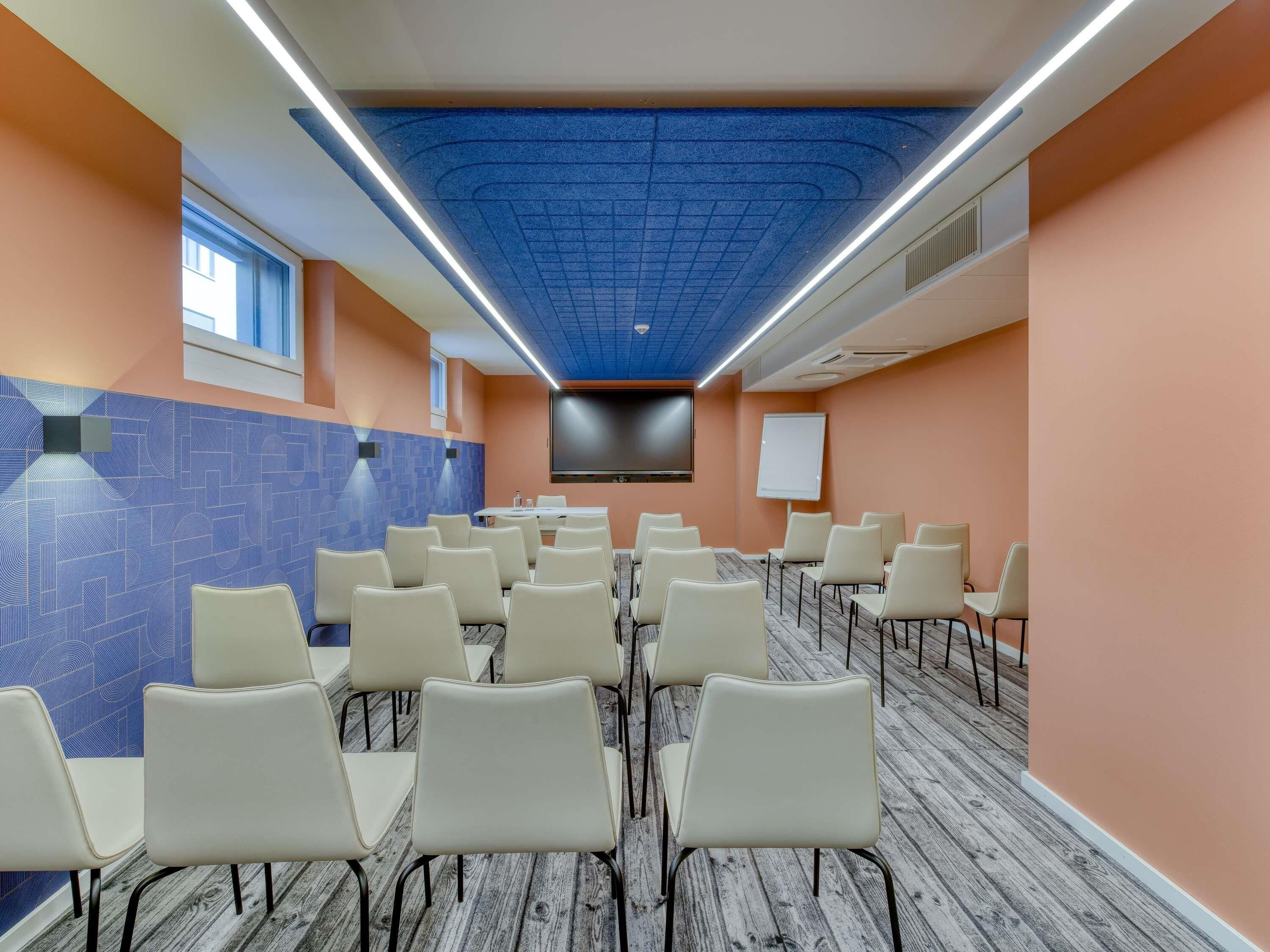 A conference room with a blue patterned wall, a whiteboard, and a flat-screen TV on the wall.