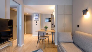 A modern living room with a sofa, a TV, a dining area with a table and chairs, and a kitchen in the background. - Aparthotel Adagio Zurich Center (Zürich)