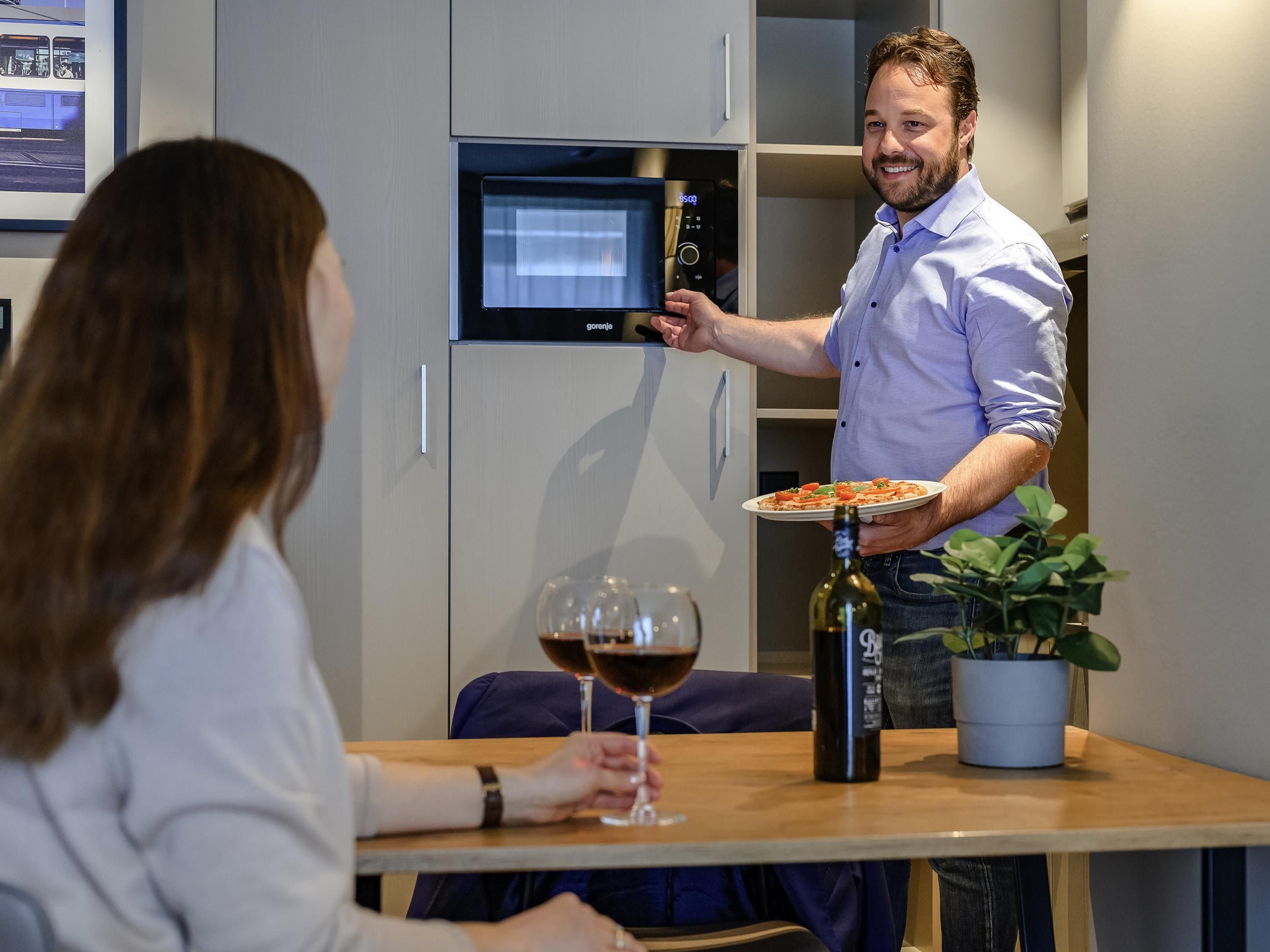 A man holding a plate of food and a wine glass in a modern kitchen setting.