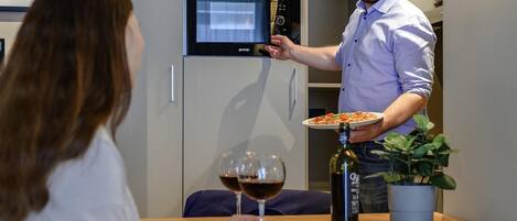 A man holding a plate of food and a wine glass in a modern kitchen setting.