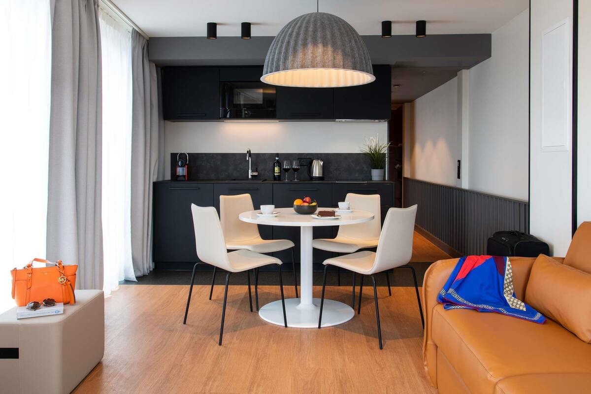 Una cocina moderna con armarios oscuros, una mesa de comedor blanca y una lámpara colgante.