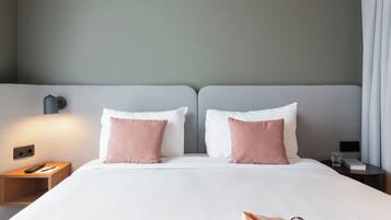 Hotelkamer met een bed, twee kussens, een nachtkastje met een afstandsbediening, een glas water en een boek.