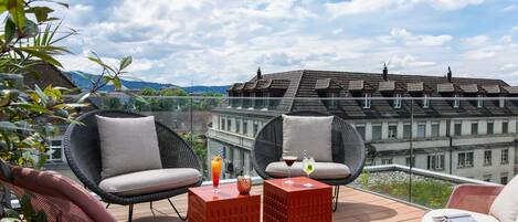 Een balkon met rieten stoelen, een rode tafel en een glas drinken.