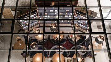 En moderne hotellobby med et centralt siddeområde, flere borde og en stor reol.