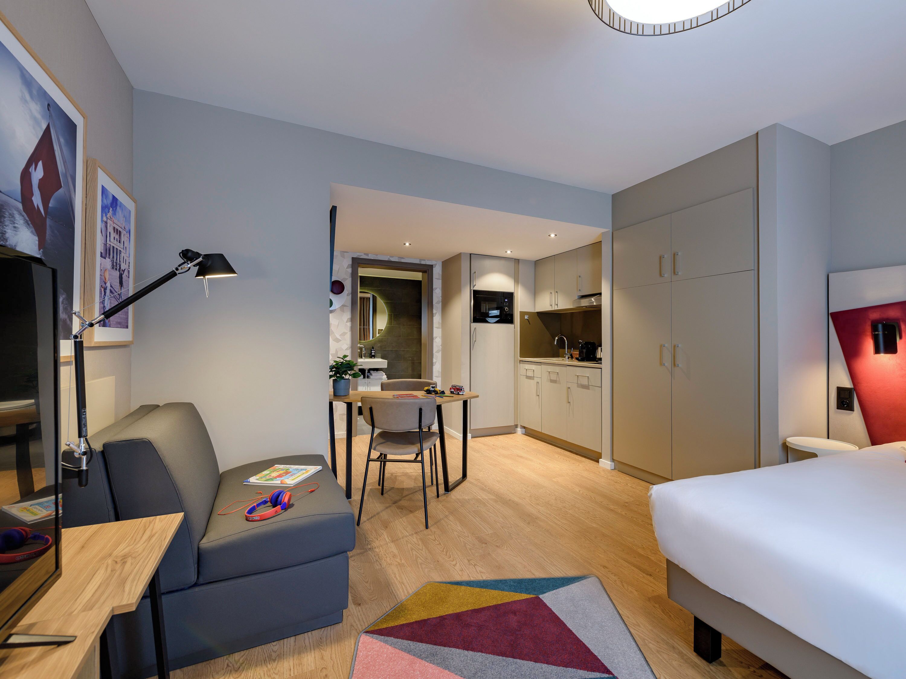 Ein modernes Hotelzimmer mit einem Bett, einem Schreibtisch mit Stuhl, einer Küchenzeile und einem Badezimmer.