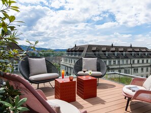 A balcony with wicker chairs, a red table, and a glass of drink. - Aparthotel Adagio Zurich Center (Zürich)