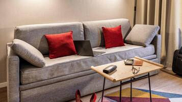 A modern living room with a grey sofa, red cushions, a laptop, a wooden coffee table, and red high-heeled shoes on the floor.