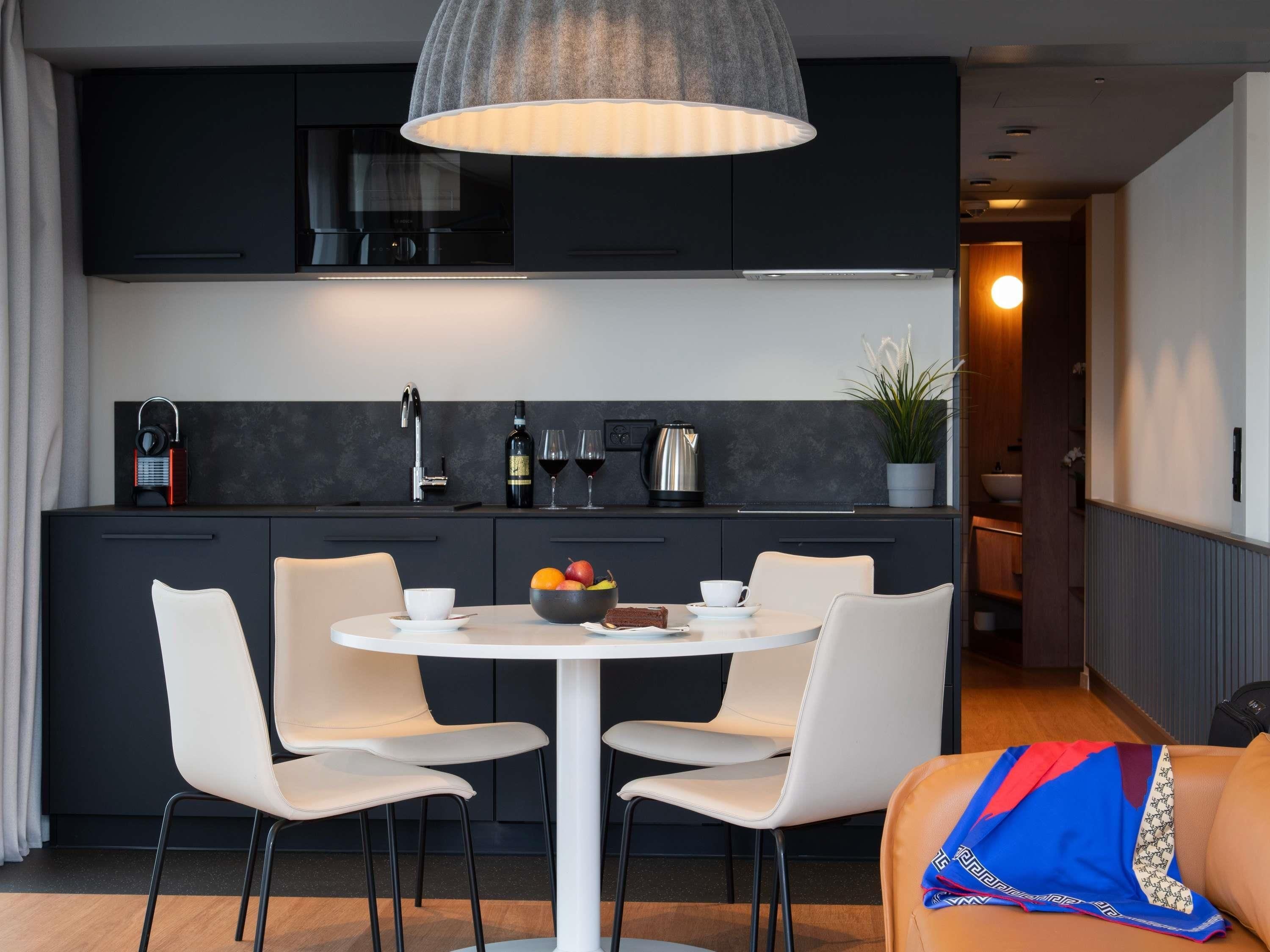 Una cocina moderna con muebles oscuros, una mesa redonda con sillas blancas y una lámpara colgante arriba.