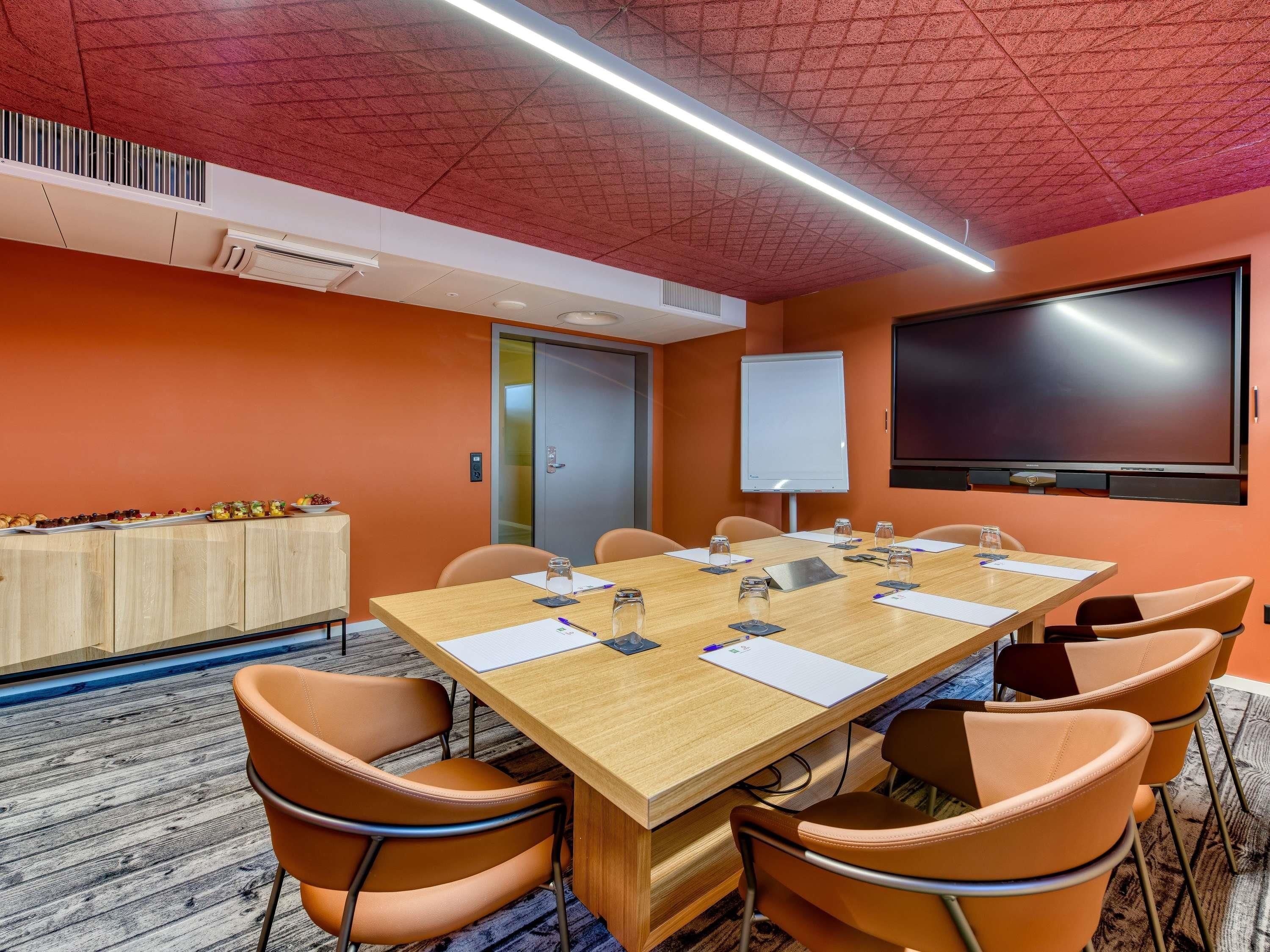 Ein Konferenzraum mit einem langen Tisch, Stühlen, einer Tafel und einem Flachbildfernseher.