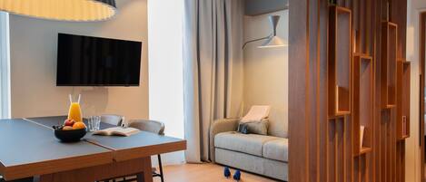 A modern living room with a dining area, a flat-screen TV, a sofa, and a wooden partition.