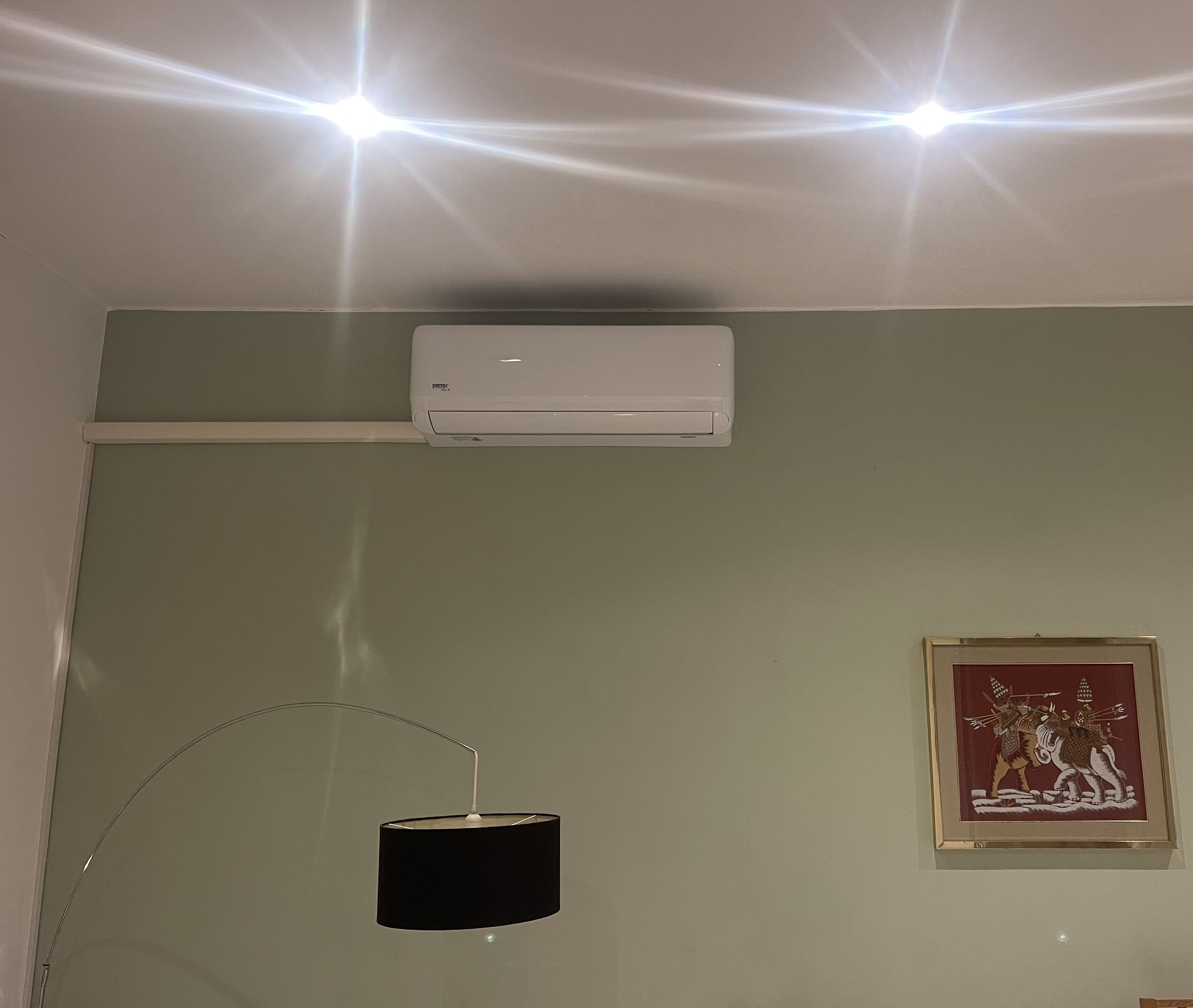 A room with a white air conditioner, a black lamp, and a framed picture on the wall.