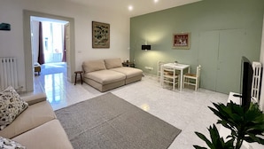 Un salon avec un canapé, une petite table et un téléviseur. Une porte donne accès à une autre pièce.