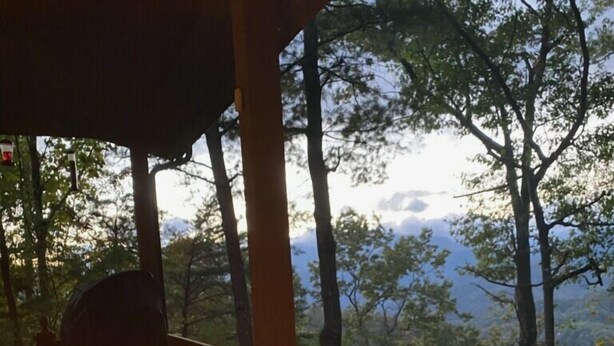 Una mesa con fogón y una copa de vino en una terraza de madera con vistas a un paisaje boscoso.