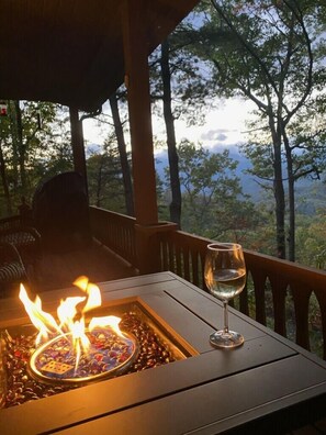 Una mesa con fogón y una copa de vino en una terraza de madera con vistas a un paisaje boscoso.