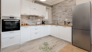 Eine moderne Küche mit weißen Schränken, einem Edelstahlkühlschrank, einem eingebauten Backofen und einer Kaffeemaschine.
