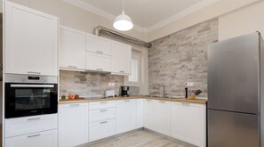 Una cocina moderna con armarios blancos, un refrigerador de acero inoxidable, horno empotrado y cafetera.