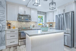 A modern kitchen with white cabinetry, stainless steel appliances, and a large island.