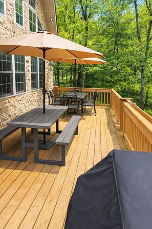 A wooden deck with a table and chairs, a barbecue grill, and a large umbrella. - Lake Harmony Chalet • Hot Tub • Pool Table • Ping Pong • Fire Pit • Pets OK (Lake Harmony)