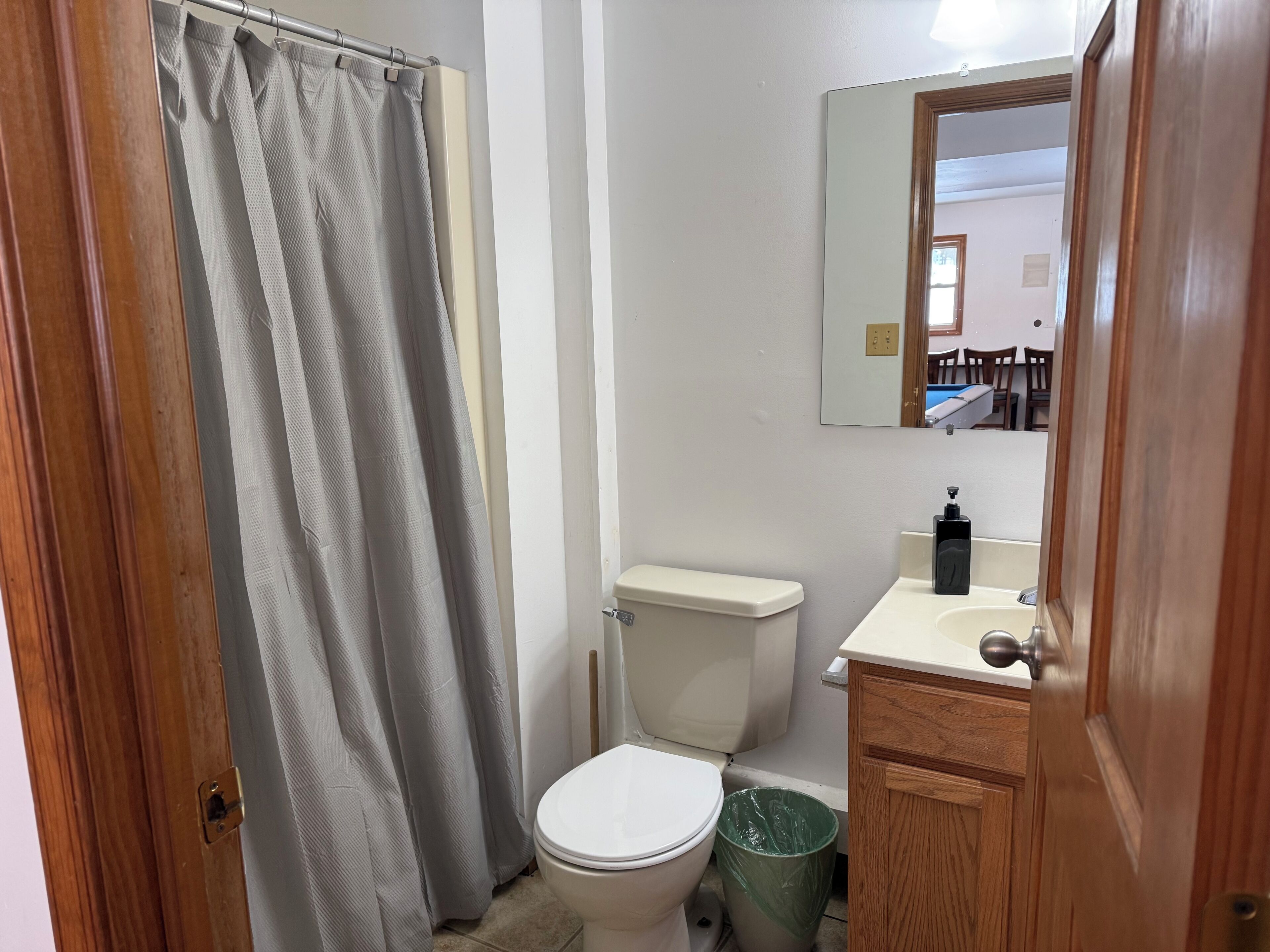 A small bathroom with a toilet, a sink, a mirror, and a shower curtain.