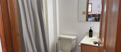A small bathroom with a toilet, a sink, a mirror, and a shower curtain.