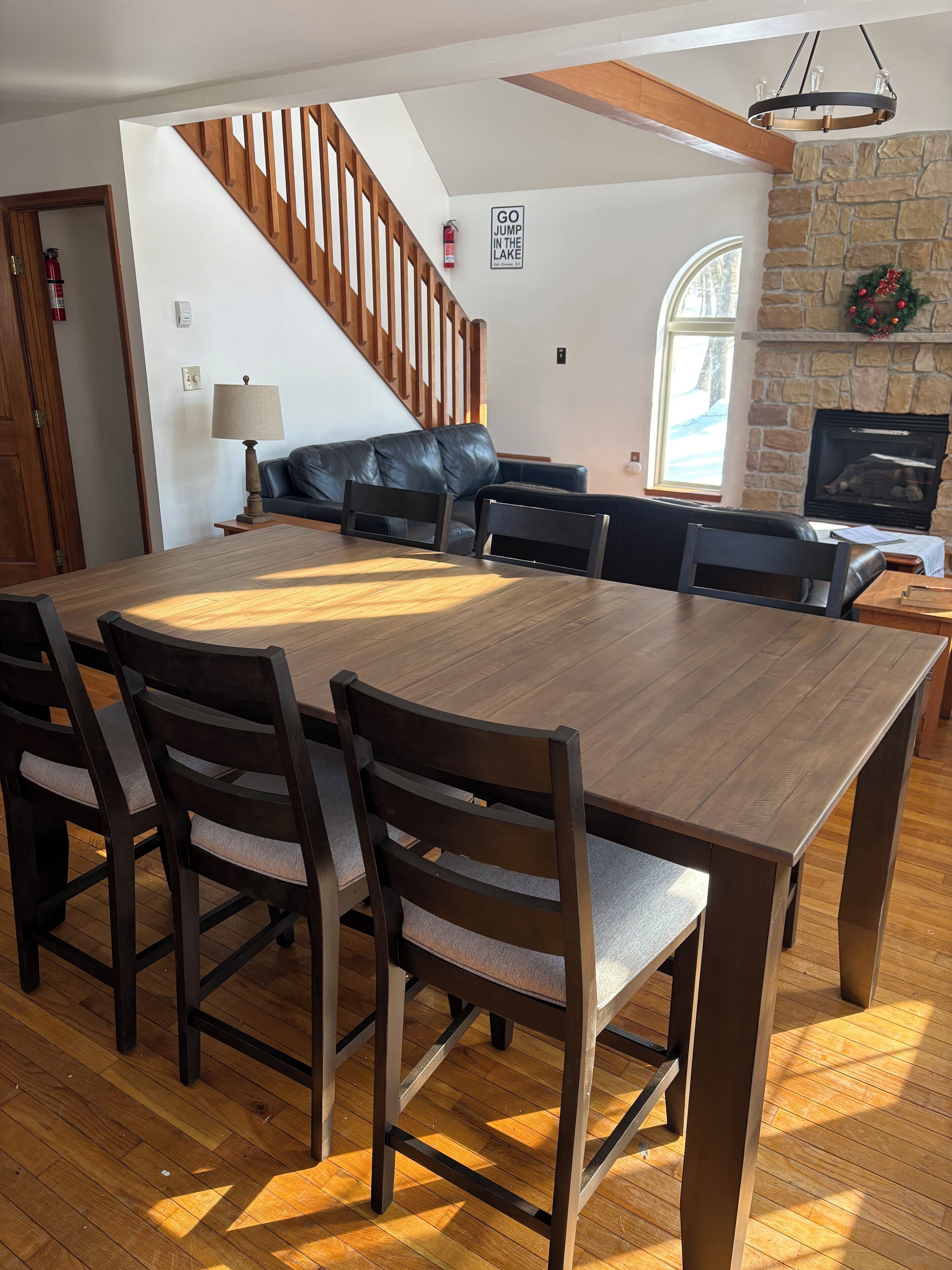 Un vaste espace dédié à la salle à manger, avec une grande table et des chaises en bois, une cheminée en pierre et un escalier menant à un autre niveau.