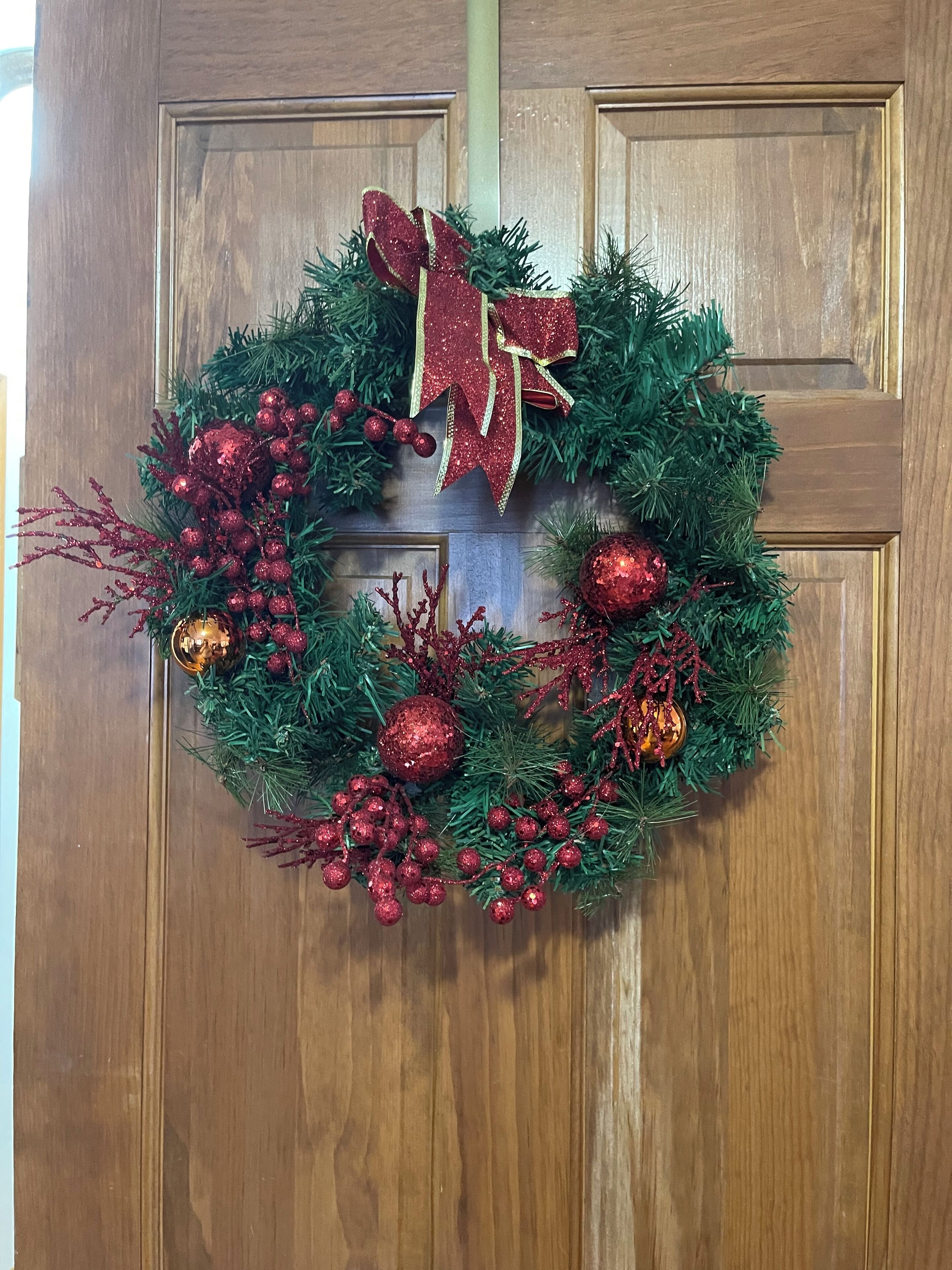 A wooden door with a Christmas wreath featuring red and gold decorations.