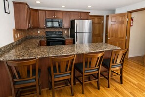 A kitchen with granite countertops, wooden cabinets, a stainless steel refrigerator, and a black stove.