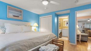 A hotel room with a bed, a ceiling fan, a door, and a view into the living area.