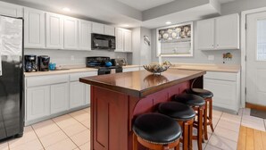 A modern kitchen with white cabinetry, a central island with stools, a microwave, and a coffee maker.