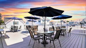 A deck with outdoor seating and umbrellas, overlooking a residential area during sunset.