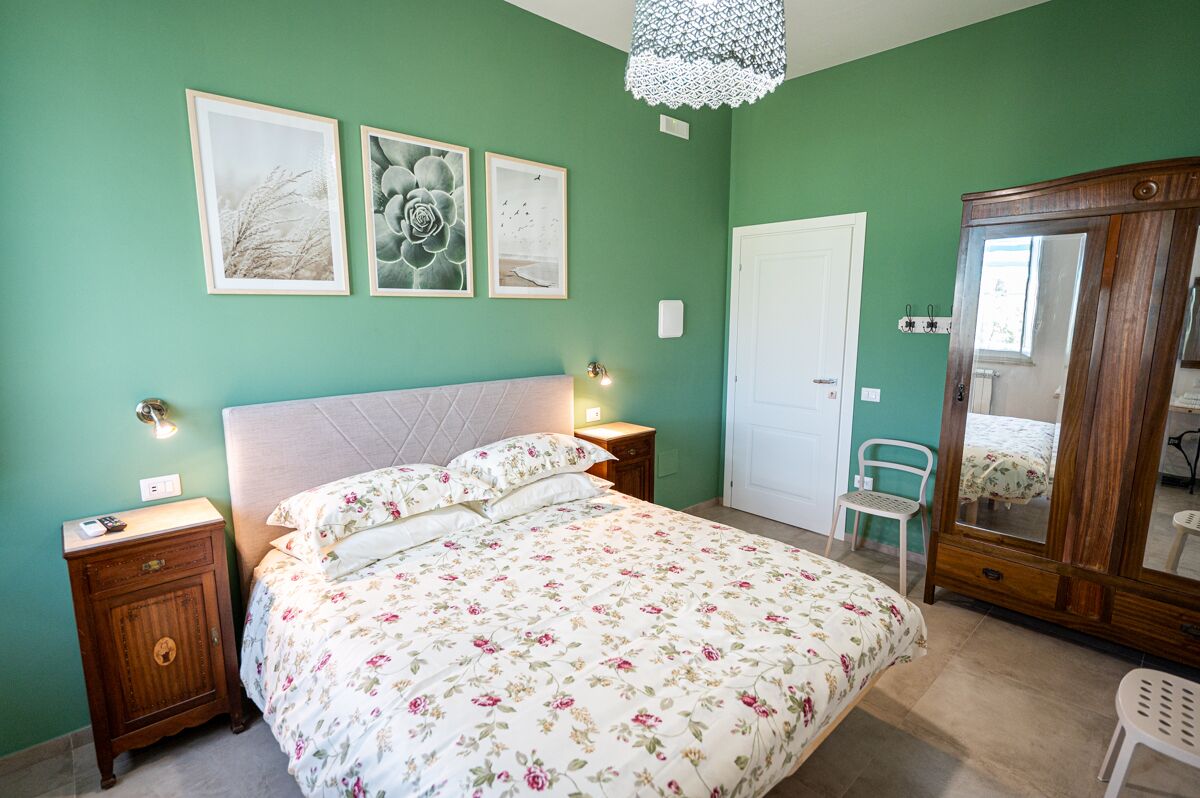 Un dormitorio con una cama, una mesita de noche, un aparador, una silla y decoración en la pared.