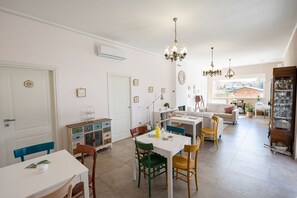 Amplia sala de estar con mesa de comedor, sillas y zona de cocina. Varias puertas y vista al exterior.