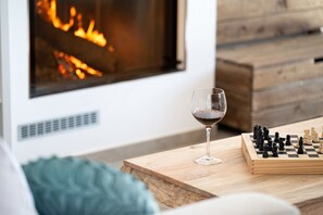 Una habitación acogedora con chimenea, un tablero de ajedrez y una copa de vino sobre una mesa de madera.