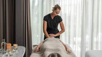 A massage therapy session in a spa room with a massage table, a massage therapist, and spa amenities like candles and essential oils.