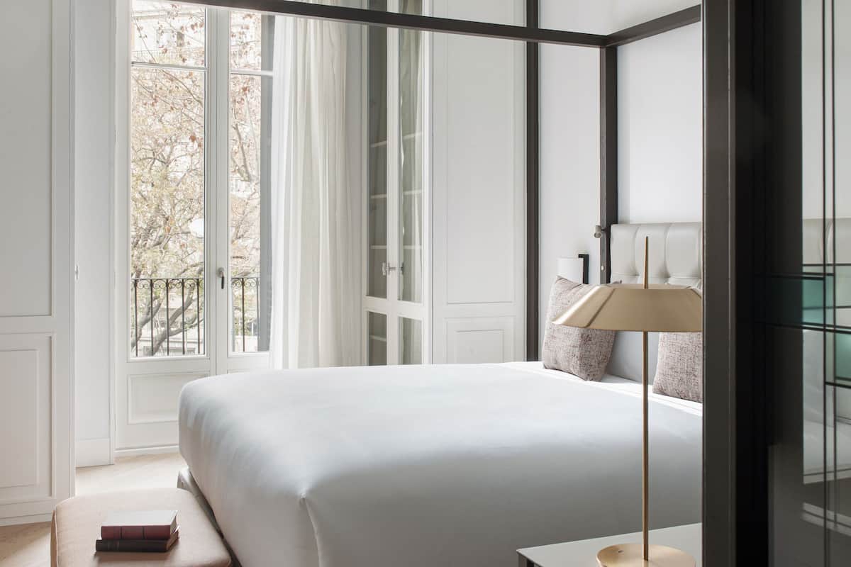 A modern bedroom with a large bed, a bedside table, a lamp, and a window with curtains.