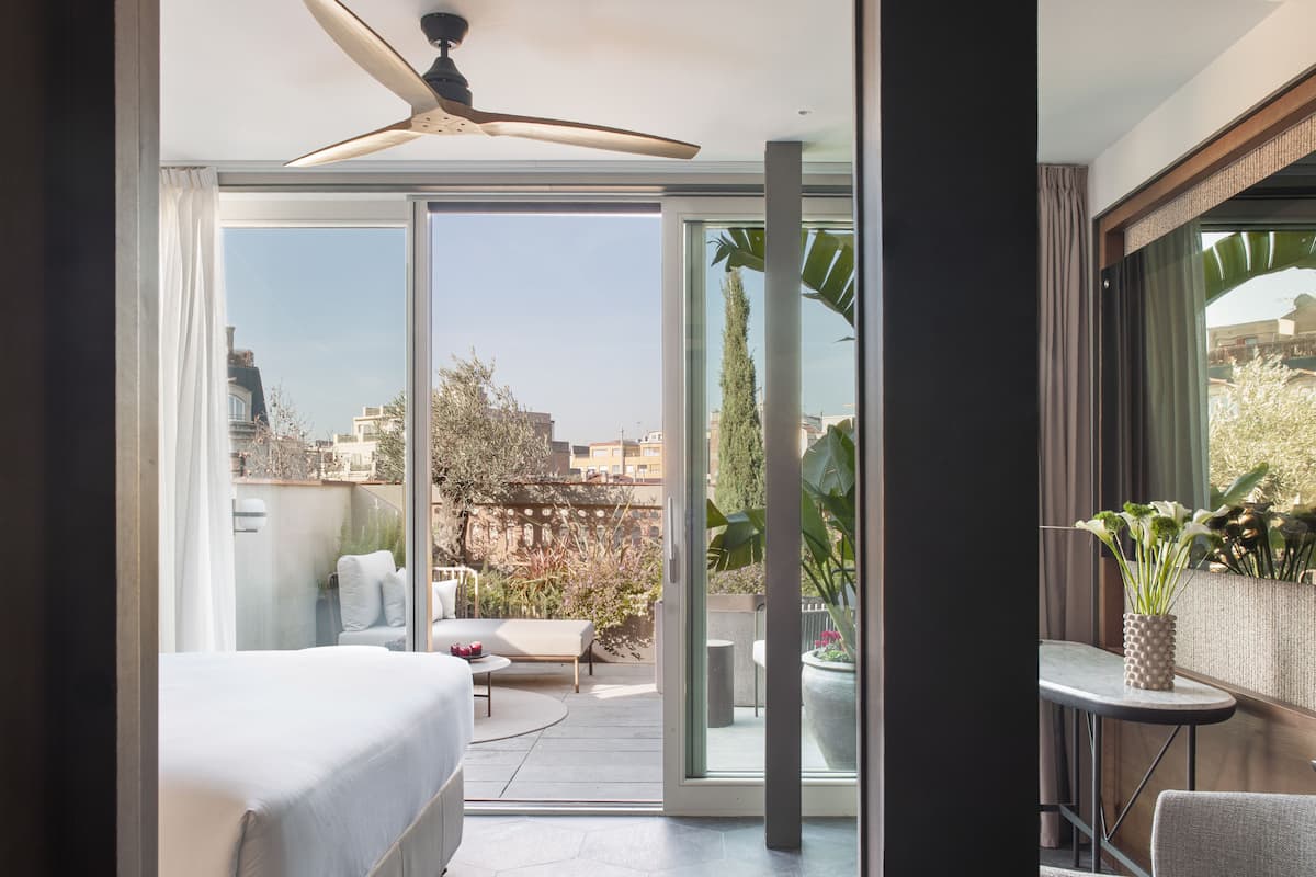 A modern hotel room with a bed, a small table, and a balcony with a view of the city.