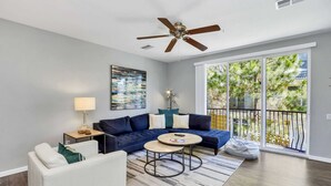 A modern living room with a blue sofa, a white armchair, a coffee table, and a ceiling fan. - Pleasant and Spacious Town Home Near the Convention Center #3vc107 (Orlando)